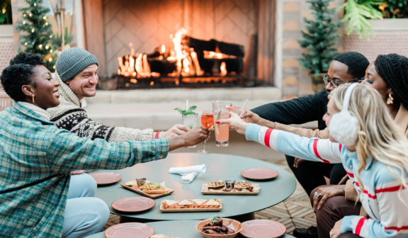 group drinking cocktails in front of a holiday fire with plates of food