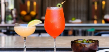 Two cocktail glasses and a bowl of olives placed on a bar counter