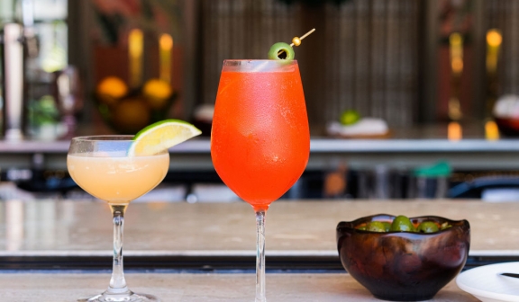 Two cocktail glasses and a bowl of olives placed on a bar counter