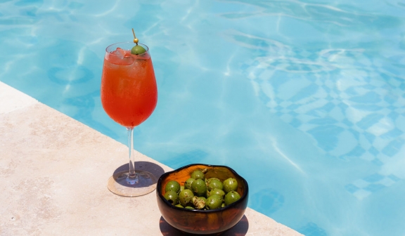 A cocktail and a bowl of olives placed on the edge of the pool