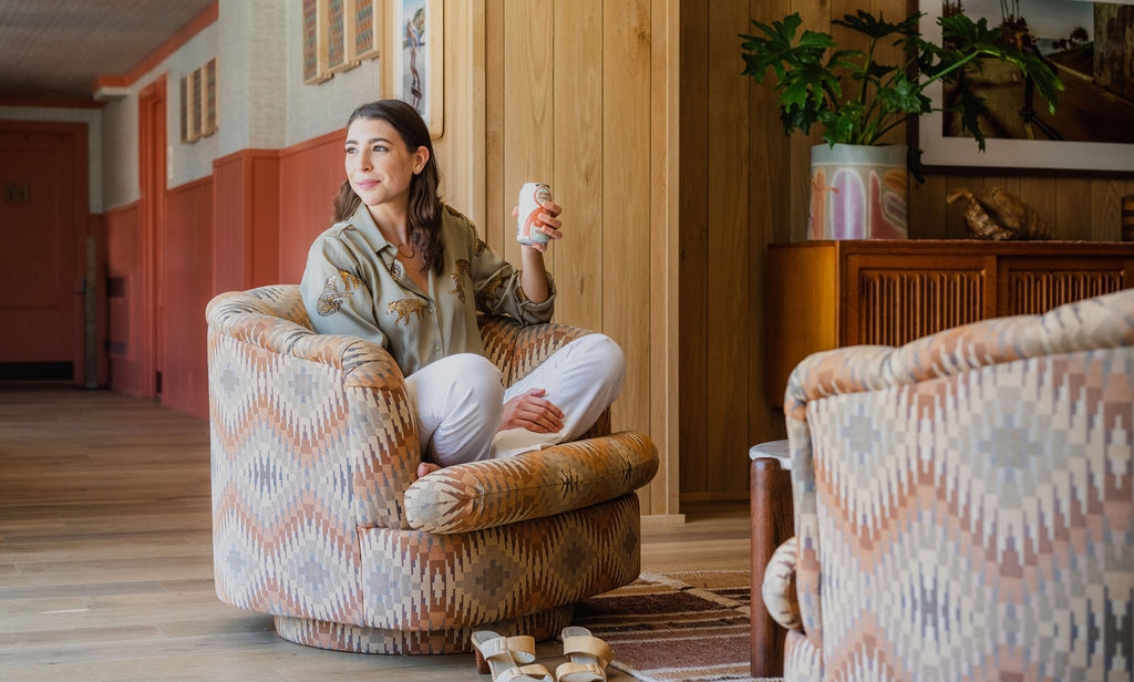 A woman sitting on a sofa chair and holding a soda can in her hand