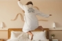 A woman in a bathrobe jumping on the bed