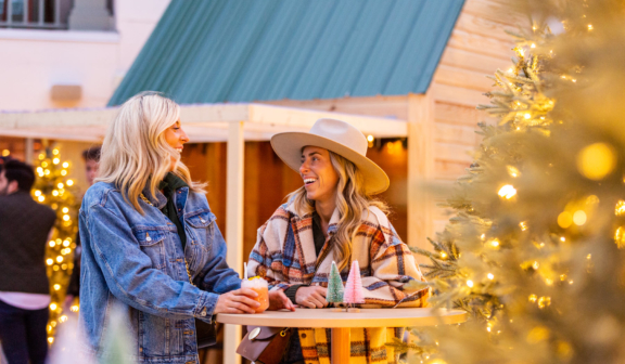 Two women laughing together at a table by a Christmas tree
