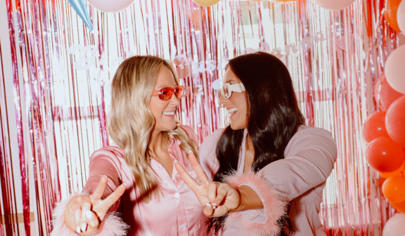 two women in pajamas having fun in front of a streamer wall