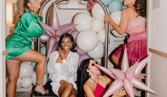 four women dressed up for a bachelorette party and hanging out on a luggage dolly