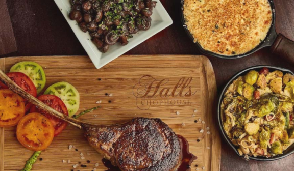 bone in steak, with sides on a butcher blocks that says Halls Chophouse